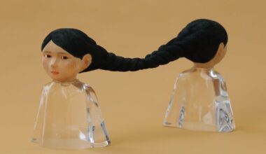 a small sculpture by Ayako Kita made of cypress and acrylic resin, depicting two female figures standing back-to-back with long black hair that is braided together