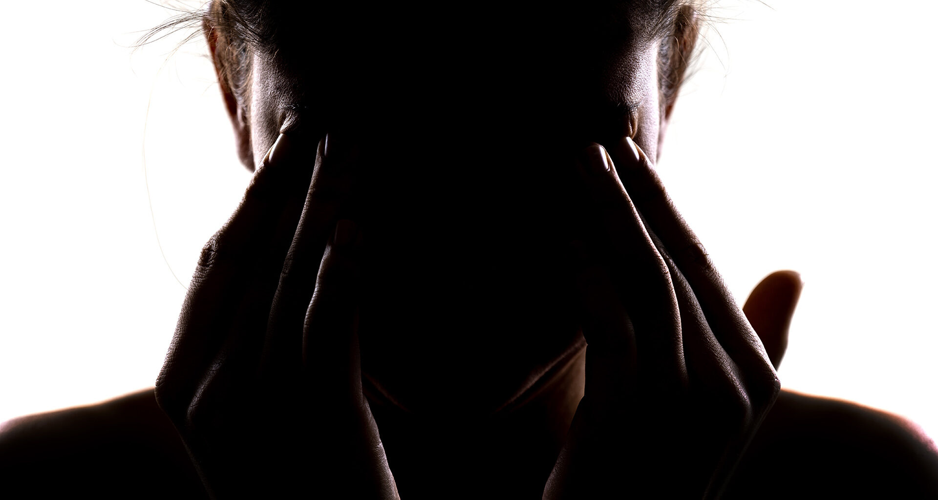 Silhouette of a person holding their head in their hands and rubbing their eyes.
