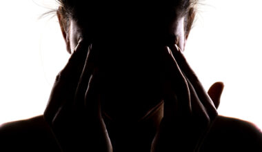 Silhouette of a person holding their head in their hands and rubbing their eyes.