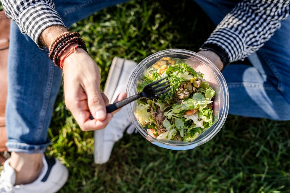 Man sitting on a meadow eating mixed salad, partial view man sitting on a meadow eating mixed salad, partial view
