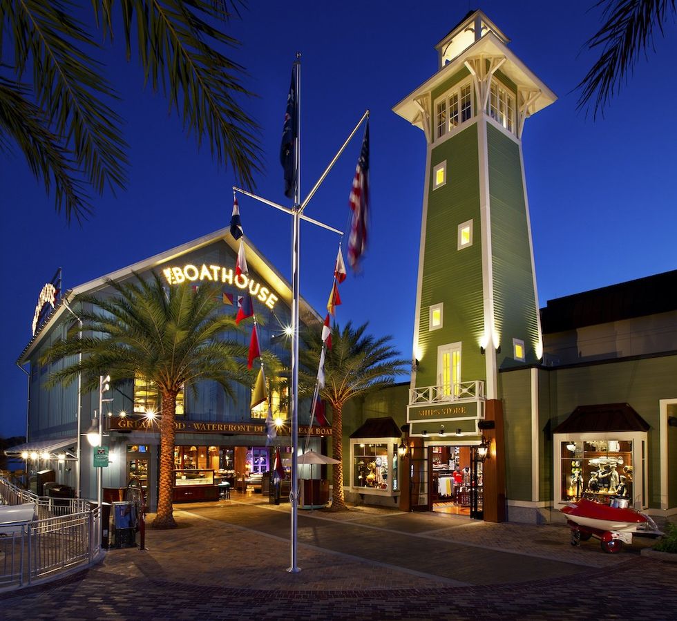 Nighttime view of a lit-up restaurant and lighthouse with palm trees and flags.