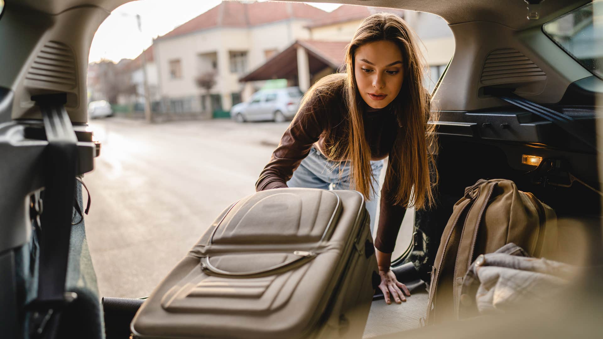 woman putting luggage filled with clothes in car trunk