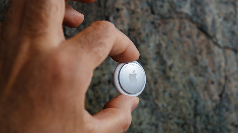 A hand holding an AirTag on a dark background