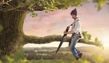 Man sitting on tree branch and sawing it off