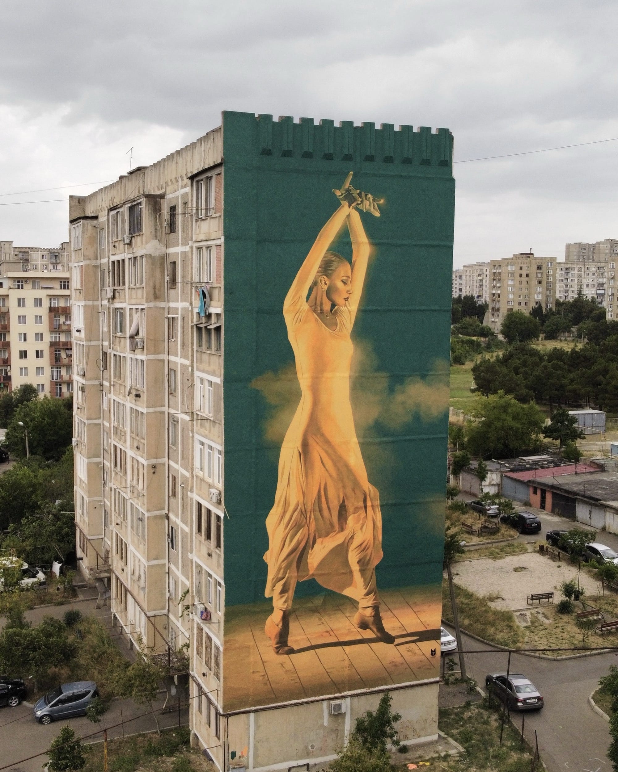 a tall mural on the side of a building of a woman dancing in a bright yellow outfit against a green background