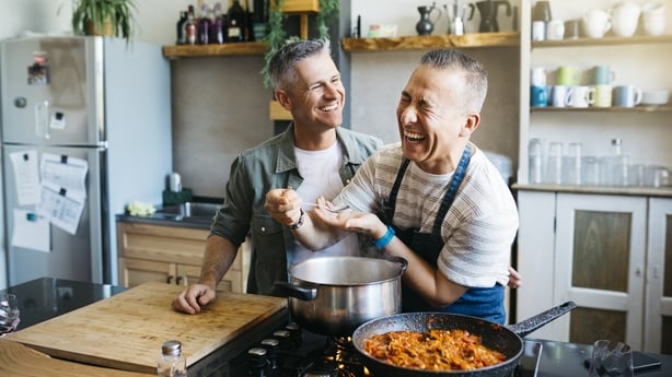 Mid adult cheerful gay couple talking and having fun while cooking in a kitchen