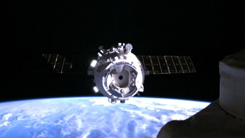 a white space capsule approaches a space station with earth in the background