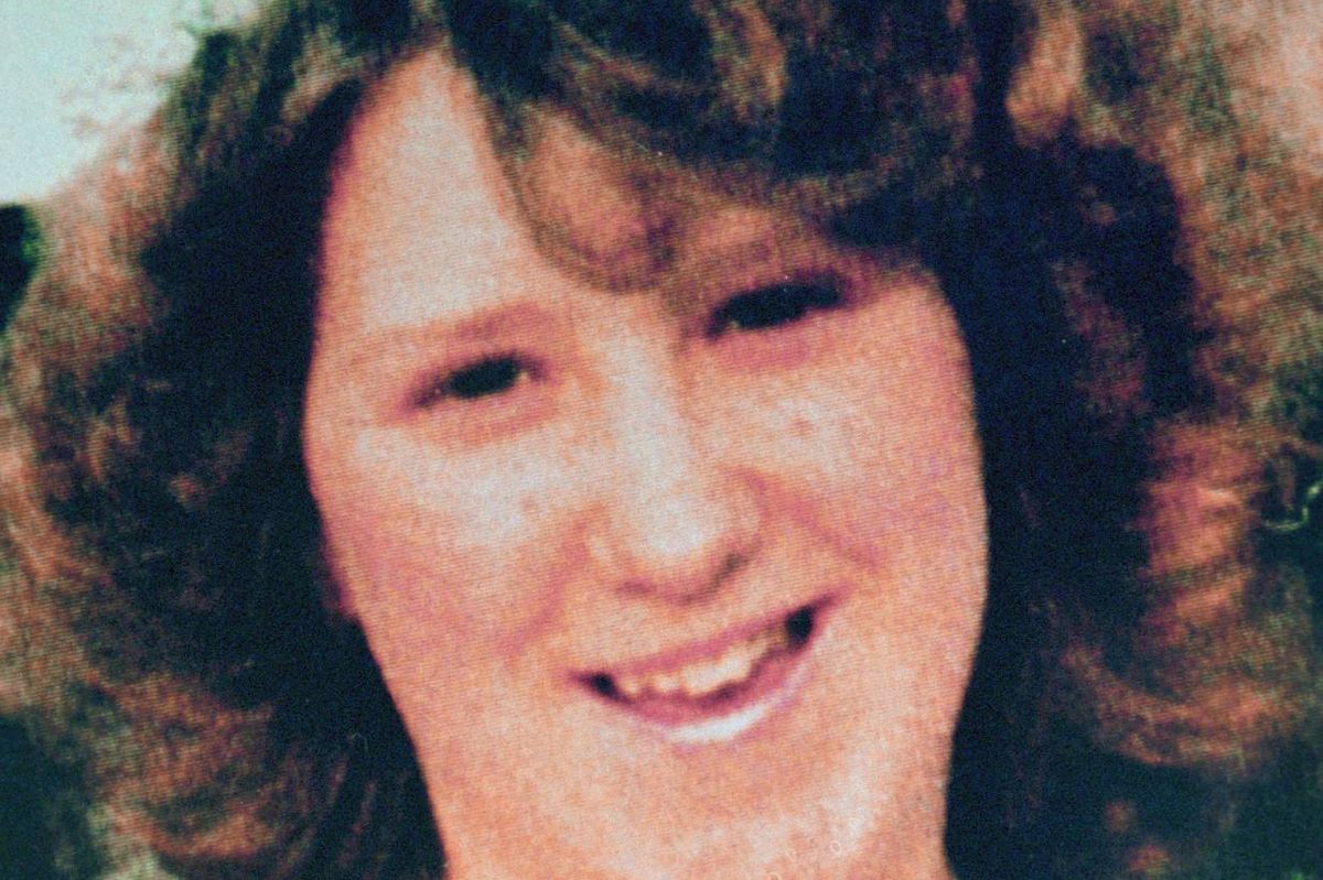 An individual with curly hair is seen in a close-up portrait, smiling warmly and displaying a cheerful expression. The individual's facial features are well-defined, and their attire suggests a formal or semi-formal setting.