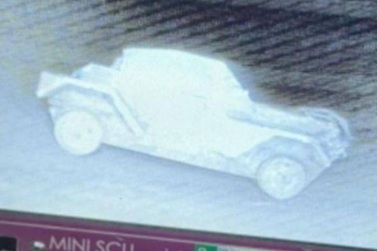A digital display screen showcases a three-dimensional rendering of a vehicle. The image appears on a monitor with a violet frame and various electronic components visible in the background.