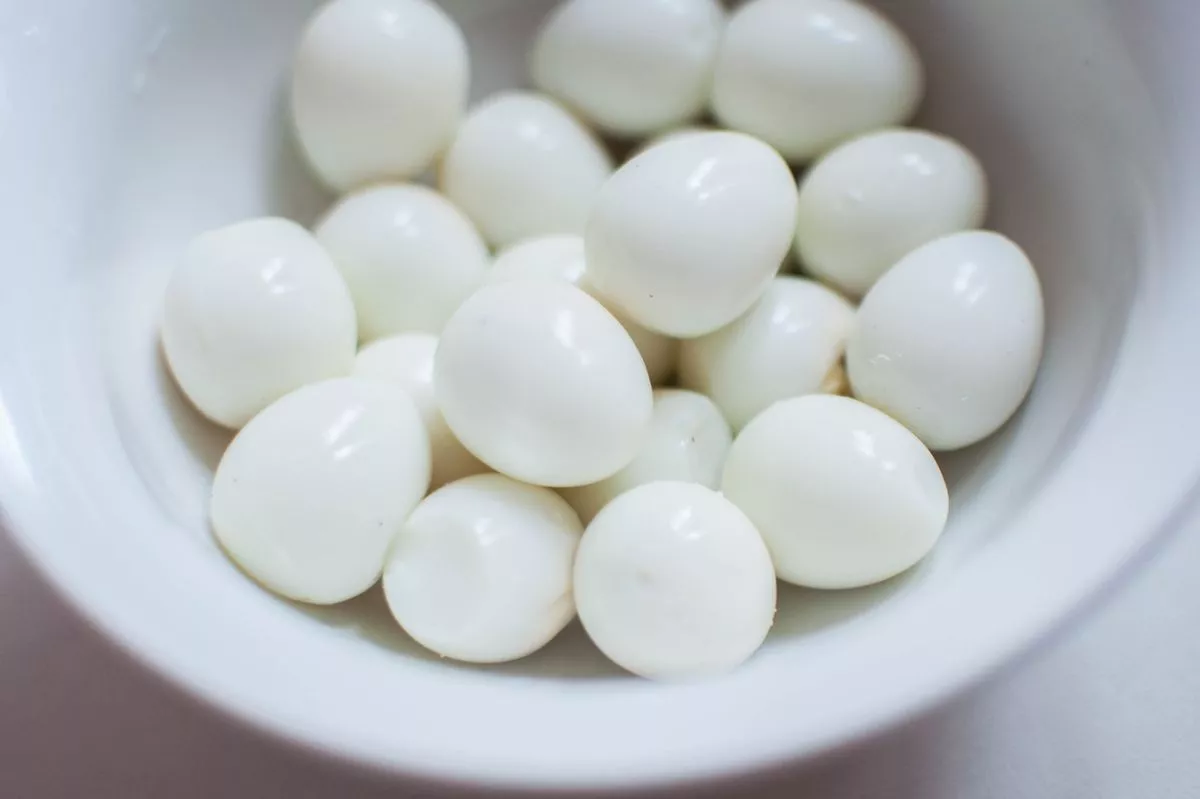 A bunch of quail eggs on a white bowl against white background