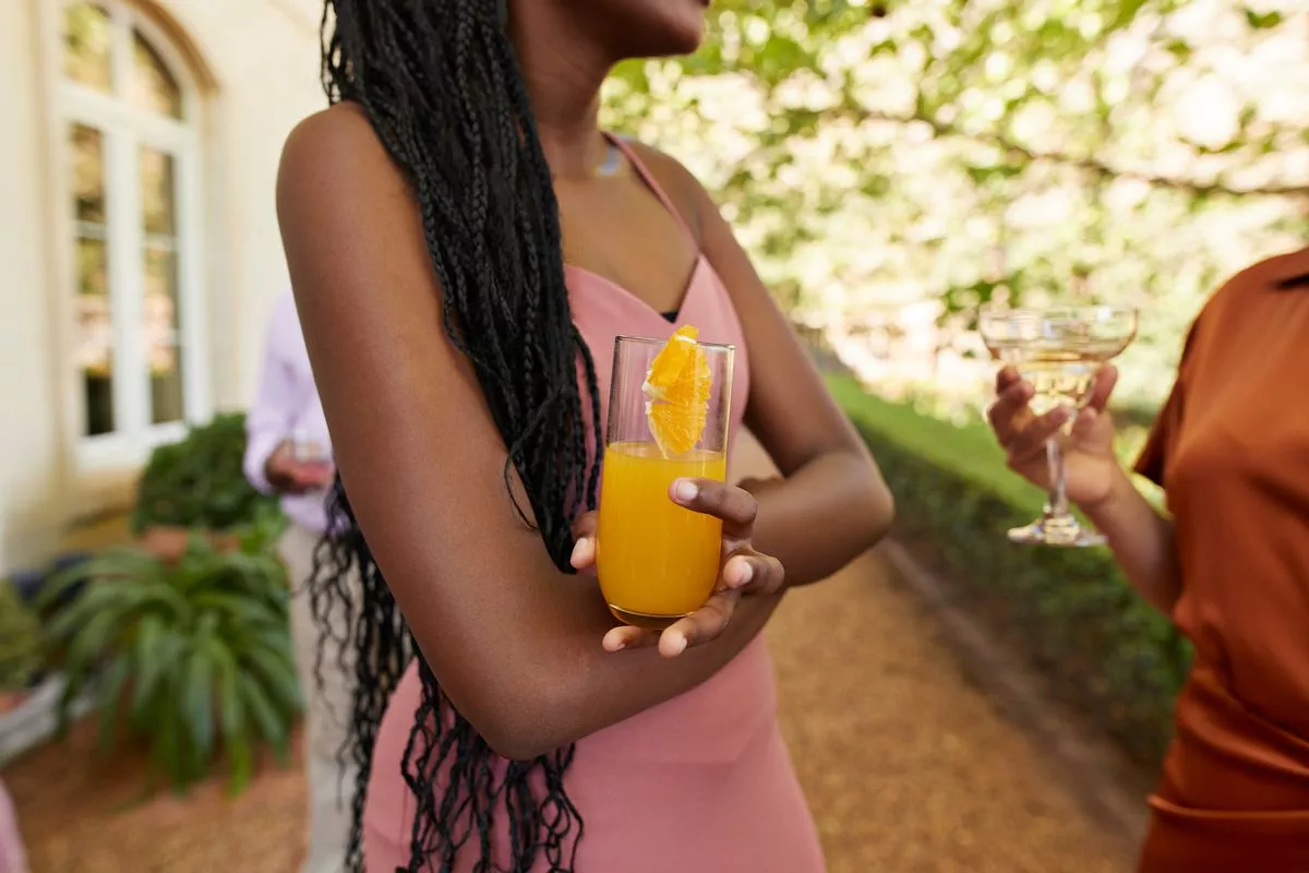Midsection of teenage girl with drink standing by female guest at wedding party