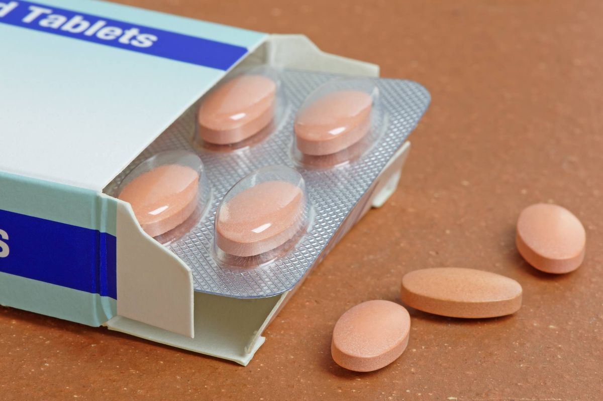 An opened blister pack containing a row of light pink tablets, with several tablets scattered outside the pack on a wooden surface.