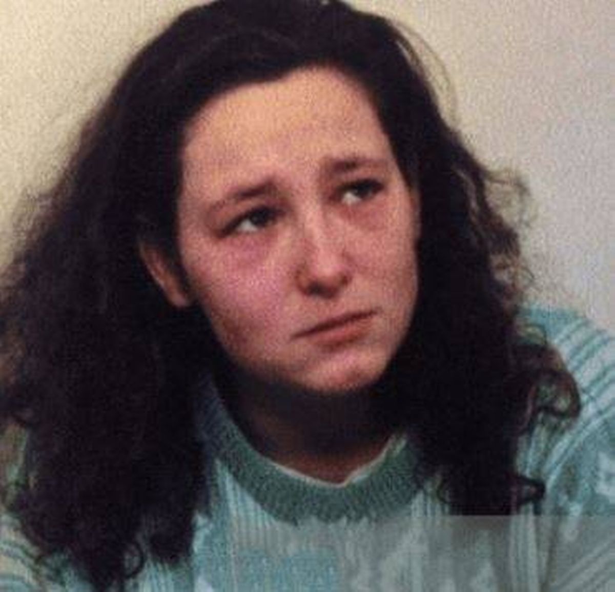 A close-up portrait of an individual with long, dark hair and a solemn expression, appearing to be engaged in an interview or court setting.