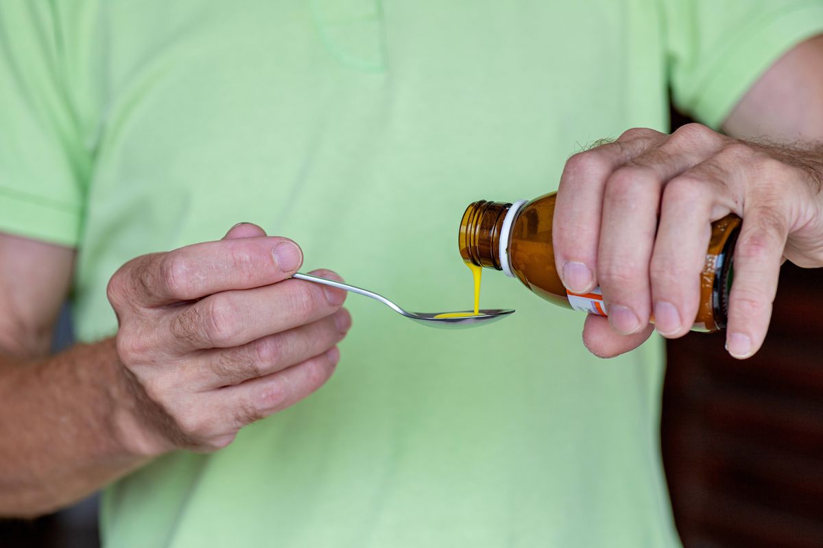 Male hands carefully pouring syrup-like medicine into a metal spoon. Concepts: home treatment, accurate dosage, family care, child and adult healthcare.