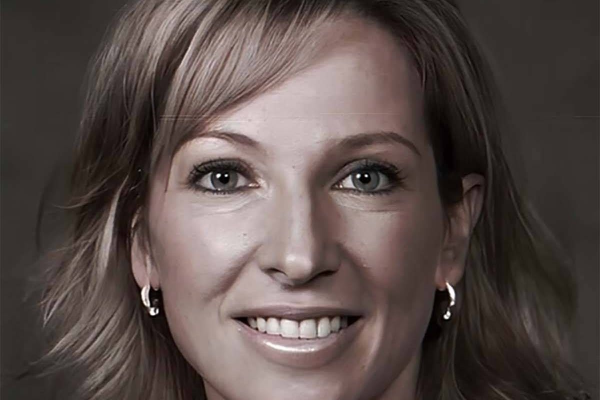 An individual with short, light-colored hair and a radiant smile, dressed in a professional manner, is captured in a close-up portrait. The subject's eyes are focused directly on the camera, exuding warmth and friendliness.