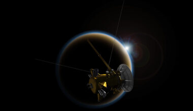 Artist's rendering of NASA's Cassini spacecraft observing a sunset through Titan's hazy atmosphere. Against the blackness of space, the moon is backlit, with a ring of white and a ring of blue light marking its outer edge, with the Sun as a point of bright light peeking from the upper-right edge of the disc. Cassini is dimly lit in the foreground partially blocking the moon, a dull gold with a large white antenna dish, and three spindly protrusions coming out of its center at 90-degree angles to each other.