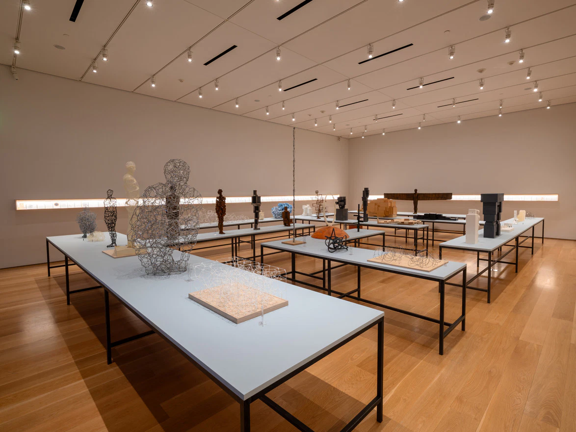Modern art exhibit in a spacious gallery with sculptures on display tables under ceiling lights.