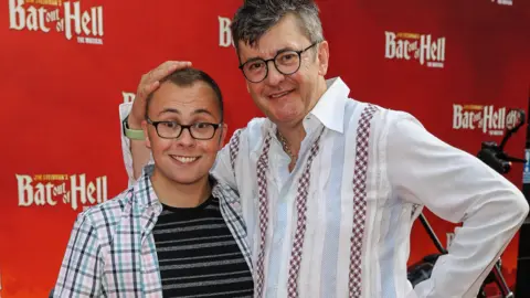 Getty Joe with his father Joe on a red carpet. They are both smiling and looking to the camera. 
