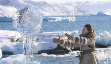 a girl in a parka, gloves and boots stands on a sheet of ice and snow with her hands out in front of her to levitate a ball of seawater into the air