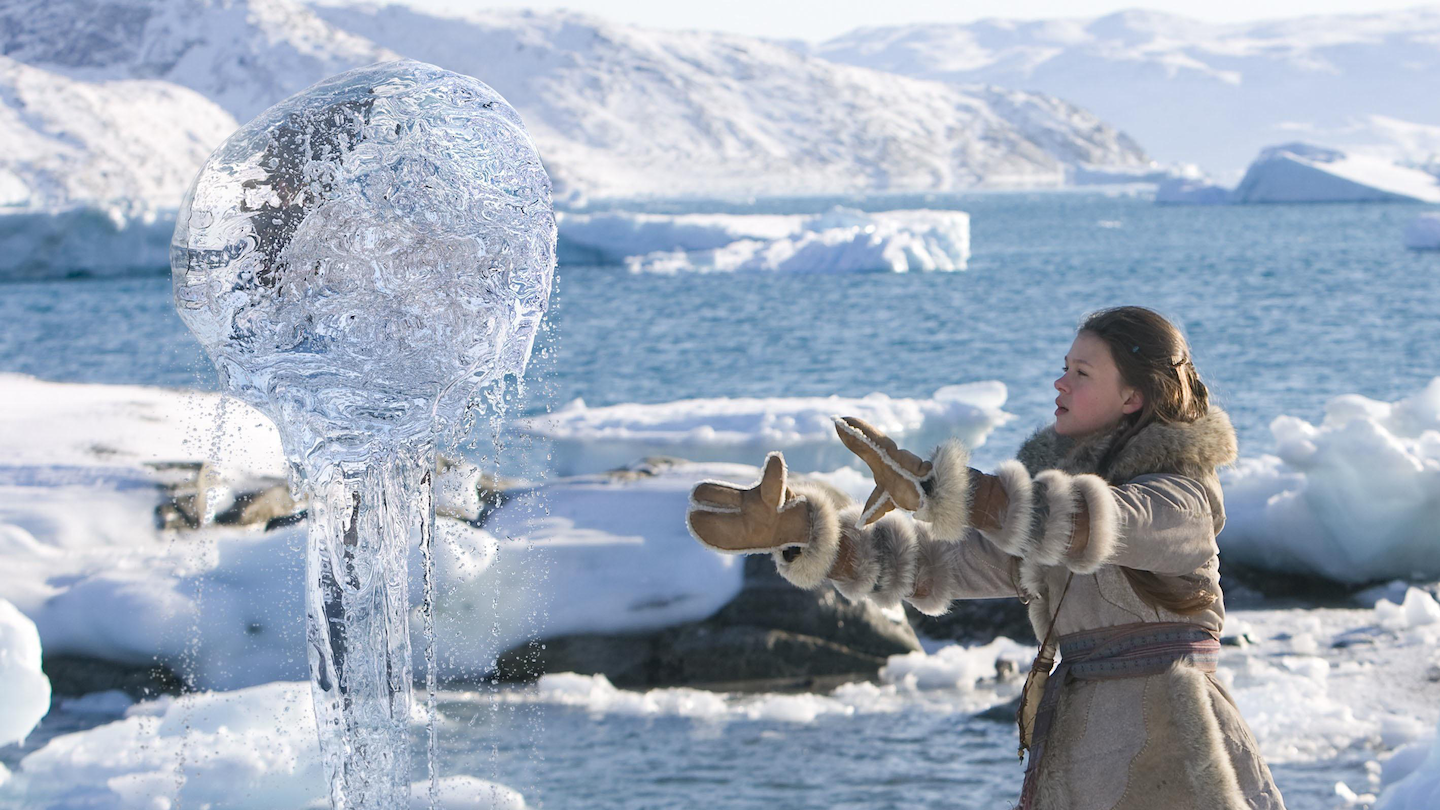 a girl in a parka, gloves and boots stands on a sheet of ice and snow with her hands out in front of her to levitate a ball of seawater into the air