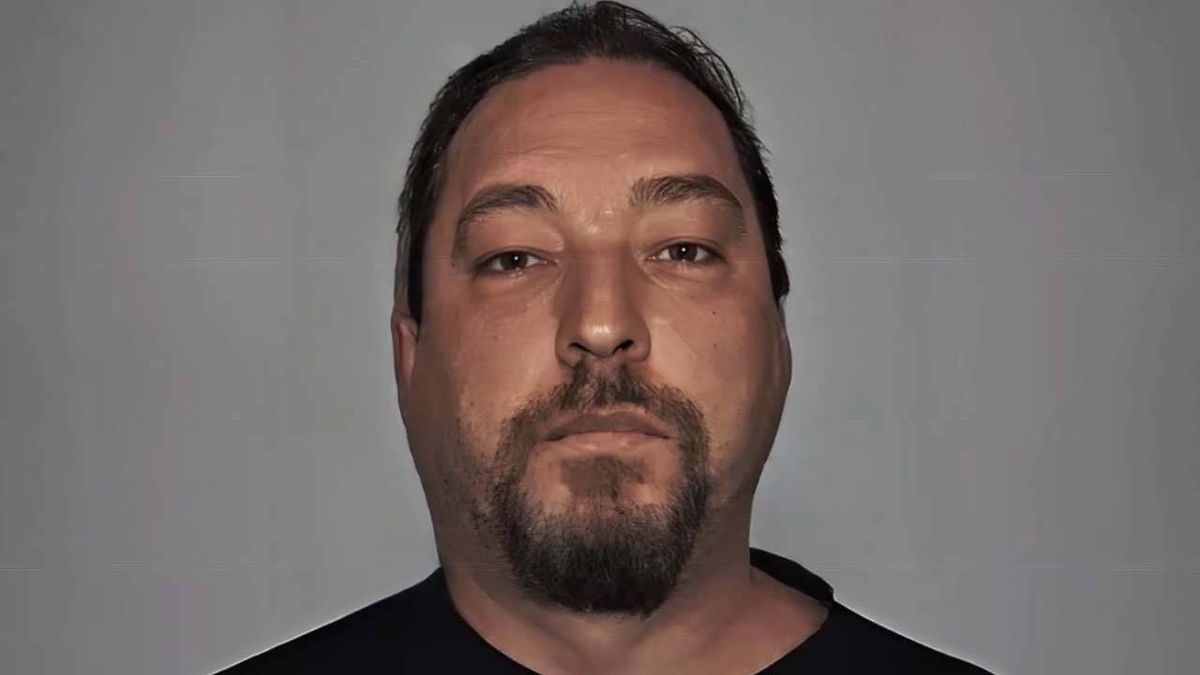 A formal portrait of an individual with a beard and mustache, dressed in a plain black shirt, against a neutral background.