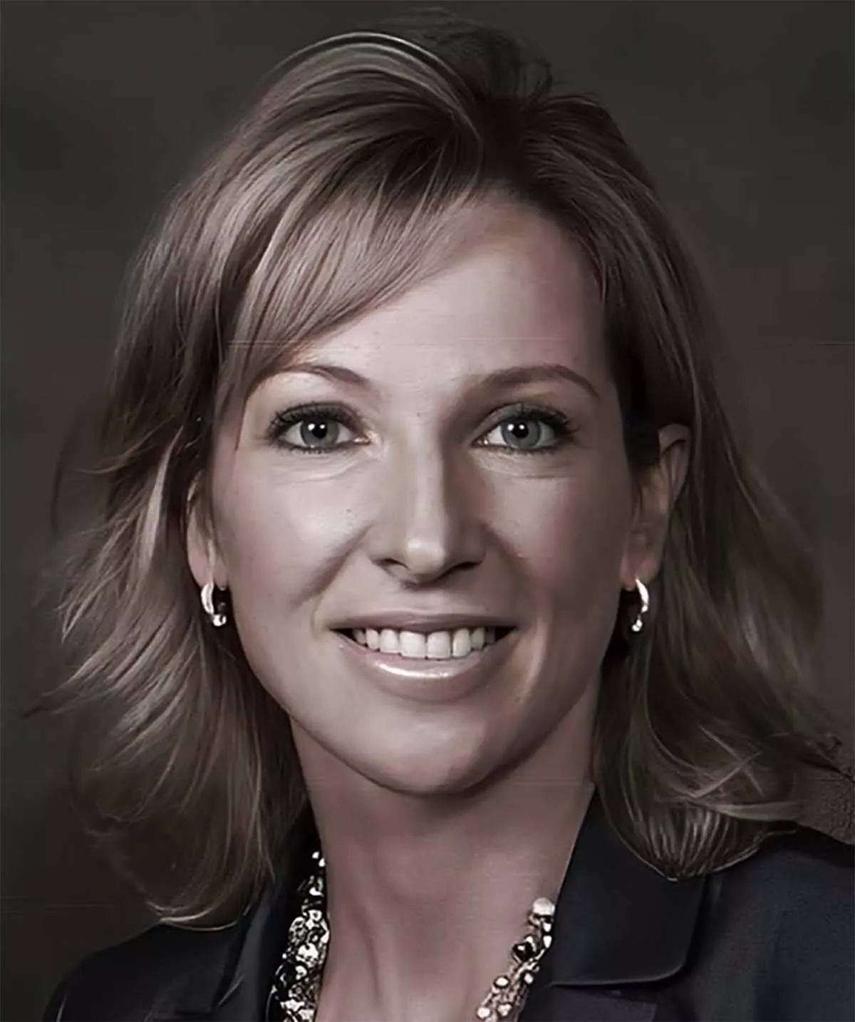 An individual with short, light-colored hair and a radiant smile, dressed in a professional manner, is captured in a close-up portrait. The subject's eyes are focused directly on the camera, exuding warmth and friendliness.