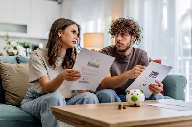 Young couple sitting on a couch at home, reviewing financial documents and talking about budget planning. Small piggy bank on table