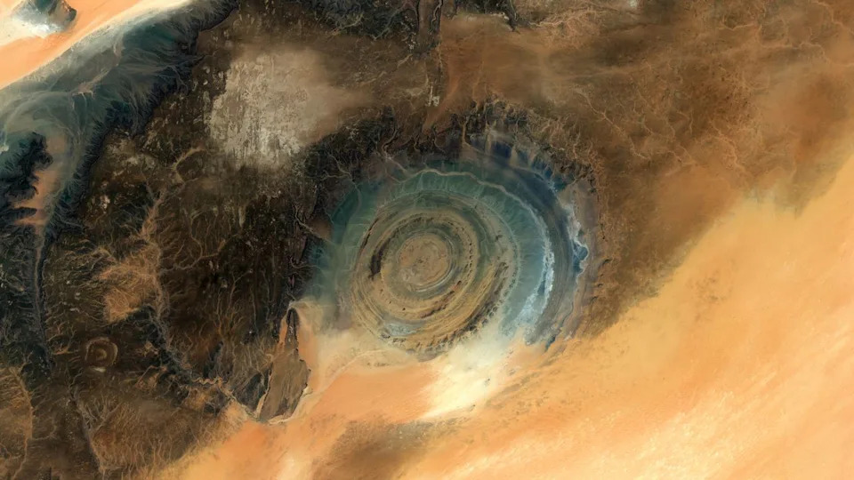 A dark circular eye peers out of a lighter landscape of the Saharan Desert.
