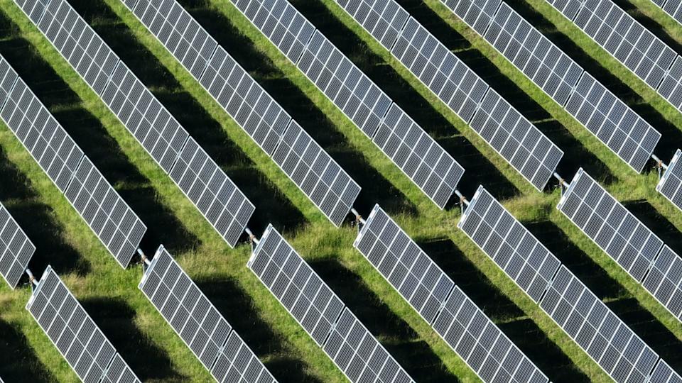 This stunning aerial view captures an array of solar panels arranged in neat, parallel rows across the landscape. From above, the panels shimmer under the bright sunlight, creating a striking contrast against the natural terrain below. The organized rows of solar panels stretch across acres of land, symbolizing the growing global shift toward renewable energy. The grid-like pattern highlights the efficiency and scale of modern solar farms, contributing to sustainable energy production.This high-resolution image showcases the incredible reach and potential of solar power as a clean, renewable energy source. Whether situated in rural fields, expansive deserts, or atop rooftops, these solar panels represent a major step toward reducing carbon footprints and combating climate change. The solar farm's orderly rows and reflective surfaces create a visually appealing scene, demonstrating both technological innovation and environmental responsibility.