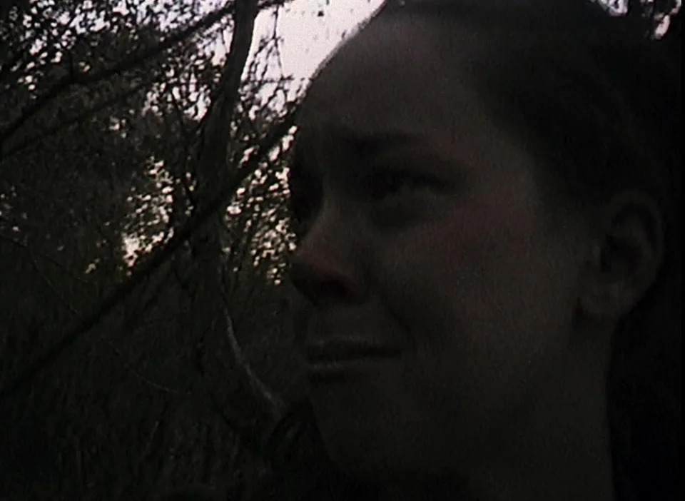 A person with a distressed expression is in a dark, wooded area, suggesting fear or urgency