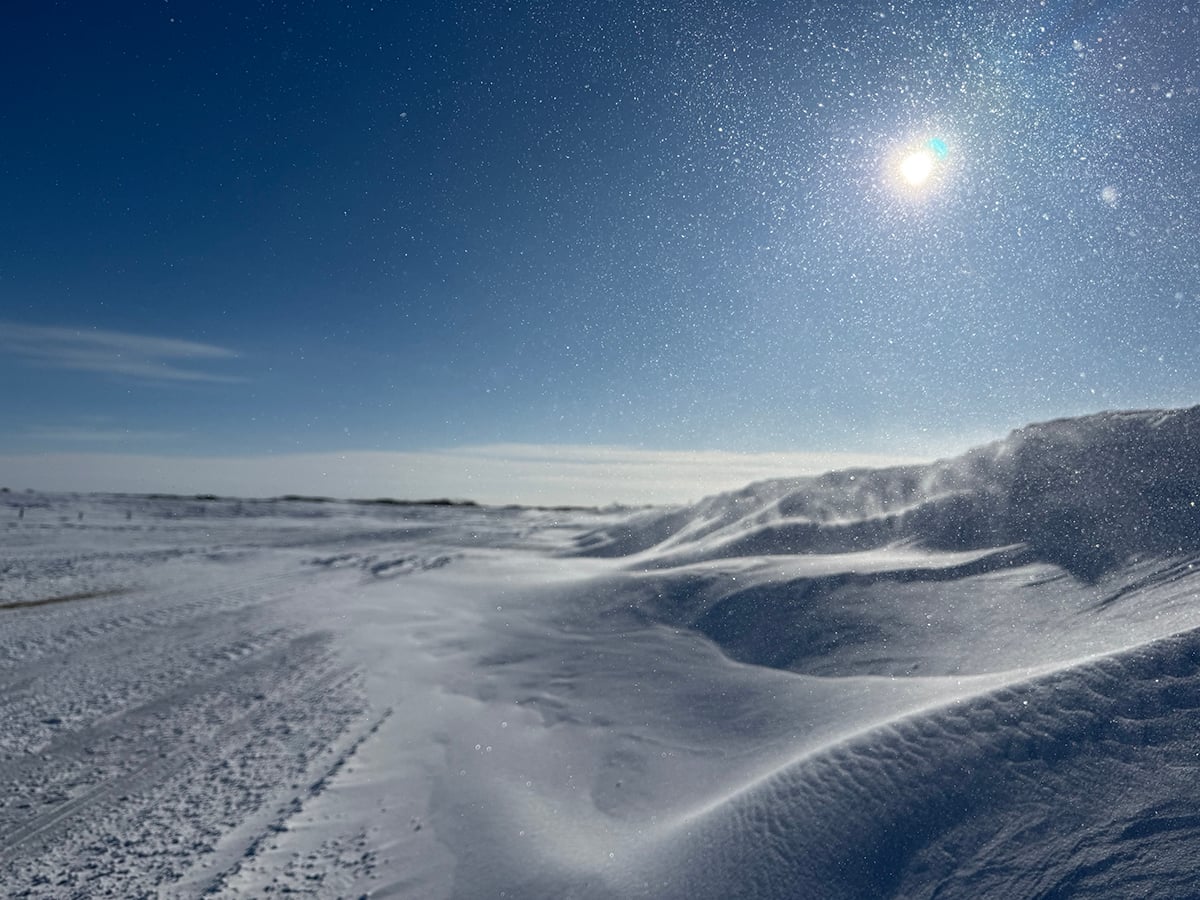 Snow is piled along the side of a road and the sun is low in the clear blue sky on a cold day in February in Saskatchewan.