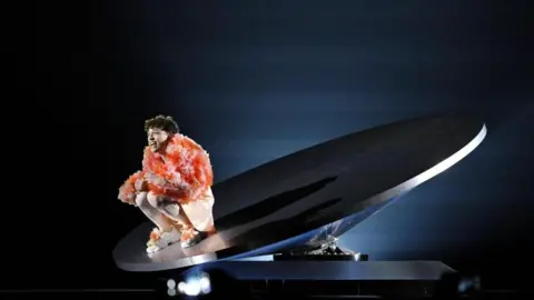 EPA-EFE/REX/Shutterstock Nemo is sitting on the stage, which has a lifted platform, wearing a bright pink, fluffy coat.