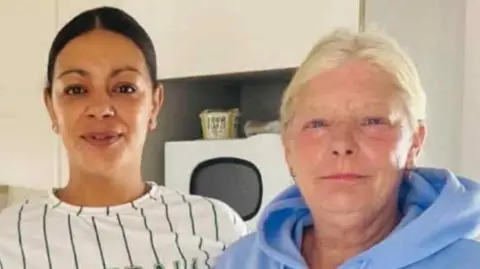 Wales News Service Belinda and Jinaise sit next to each other. Both have their hair up. Jinaise has dark hark and is wearing a round neck white shirt with green vertical strips. beline is wearing a light blue hoodie with the hood down 