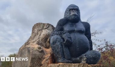 A large gorilla statue sitting on a tree stump as viewed from below.
