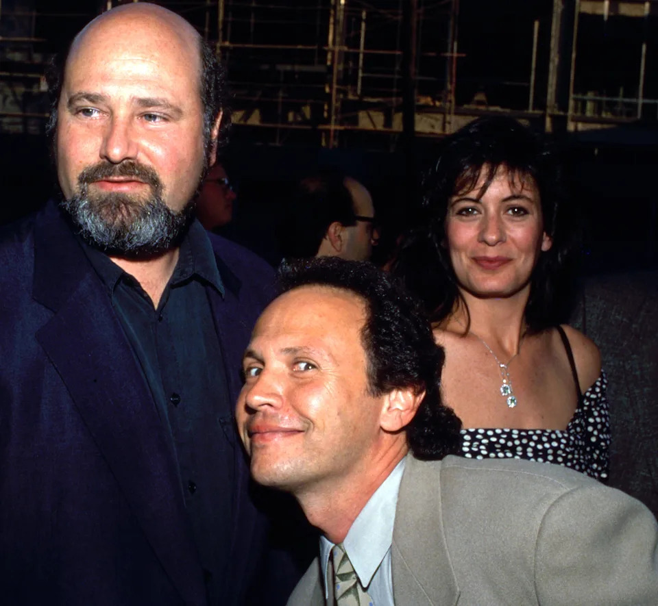 Group of people posing at an event; one person is wearing a suit jacket, another a patterned dress, and a third smiling in a suit