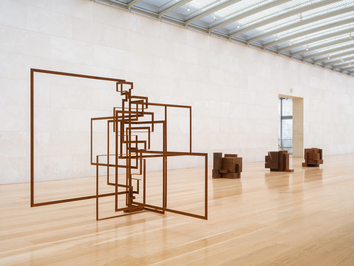 Modern art sculpture installation in a bright gallery with wooden floors and high ceiling.