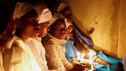 Reuters Women hold candles as they attend a Christmas Eve mass in Nairobi, Kenya on 25 December 2025.