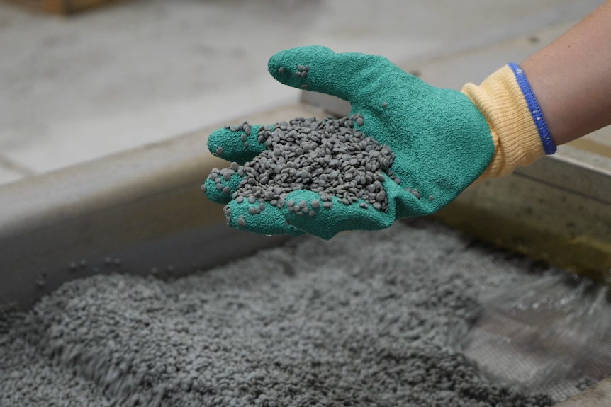 Grey pellets sitting in a person's hand, made from recycled plastic.