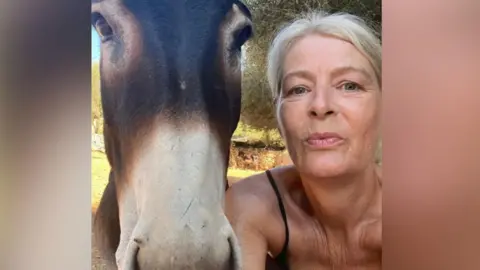 Menorca Donkey Sanctuary A donkey with a white nose stares into the camera, with a woman stood by him.