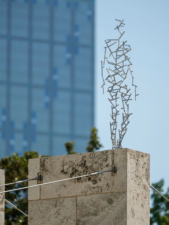 Sculpture of metal rods shaped like a human figure on a building edge, city skyscraper in the background.