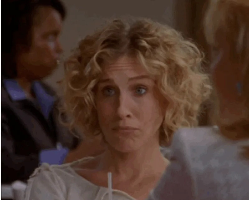 Person with wavy hair sipping a drink looks contemplative while seated indoors