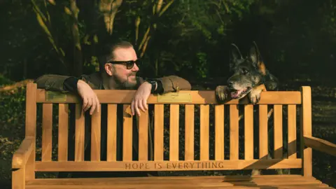 Submitted Ricky Gervais posing with a German shepherd dog in a publicity still for After Life.