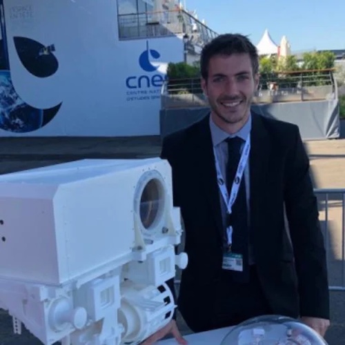 Smiling man wearing a dark jacket and lanyard standing next to a replica of a Mars rover.