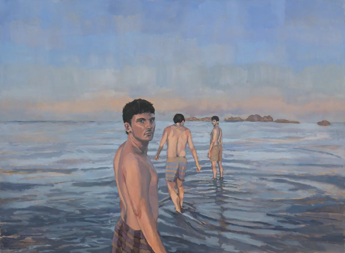 Three men walking in shallow ocean water with a hazy horizon under a blue sky.