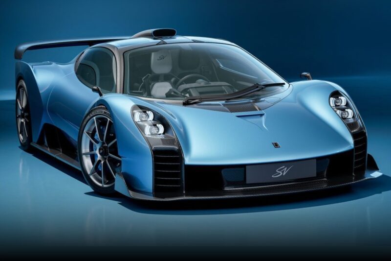 A blue sports car with aerodynamic design, prominent front headlights, large rear wing, and black alloy wheels is shown against a blue background—one of the 20 Cars That Focused on Analog engagement in 2025.