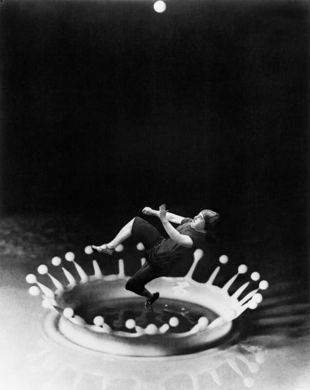 A black-and-white surreal image showing a person floating above a giant water droplet crown splash, with a small ball suspended above them in a dark, empty background.