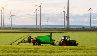 A tractor on a open field with windmills in the background.