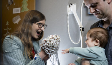 A parent holding a child, who reaches out for a researcher holding an EEG cap