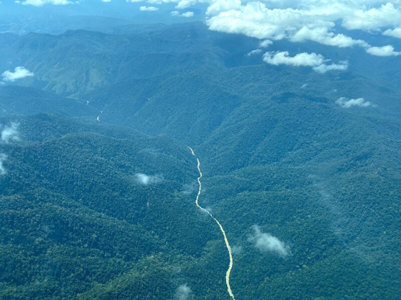 A view from an airplane looking down at thickly forested hills and a river running through the valley.