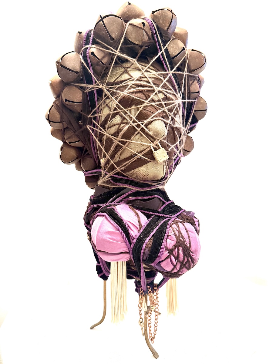 A sculpture of a head wrapped in fabric and rope, with a crown of rusted jingle bells bound together with yarn.